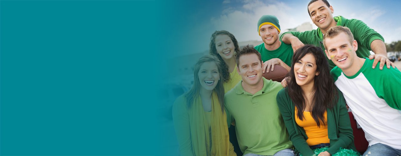 Group of young people smiling and sitting outdoors, dressed in casual green and yellow sports attire, holding a football.